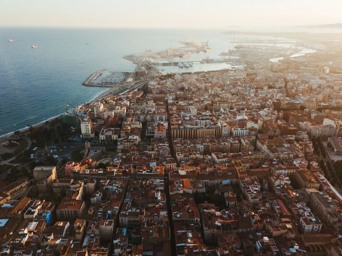 Tarragona vista desde el aire al atardecer: los tejados del casco antiguo, la ciudad hasta la costa y el puerto con sus grúas al fondo.